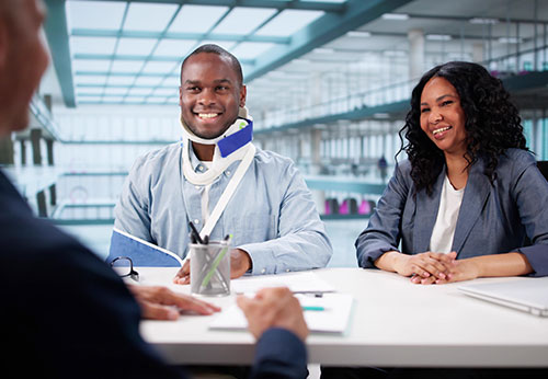 Happy lawyer and injured client in a neck brace discussing a personal injury claim