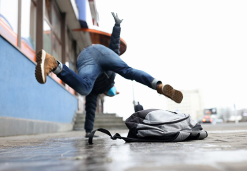 A person in mid-air falling backward on a sidewalk next to a backpack, illustrating a sudden slip and fall accident.